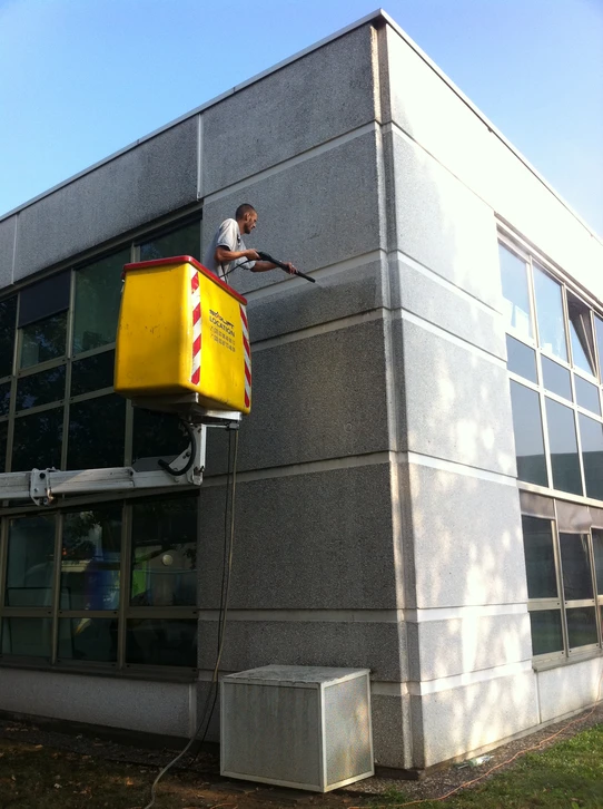 Chantier extérieur avec grue mobile jaune soulevant une nacelle élévatrice noire à plateforme de travail