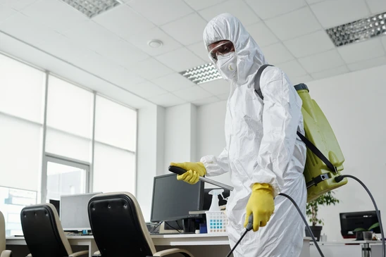 Personnel en combinaisons de protection intégrale blanches désinfectant un bureau moderne