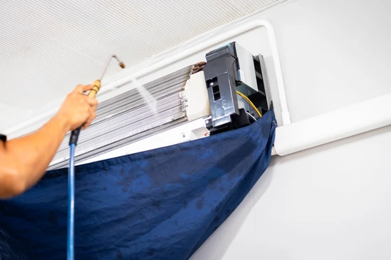 Technicien en tenue professionnelle et équipement de protection (gants, masque si approprié) intervenant dans un espace intérieur partiellement endommagé montrant des traces visibles de sinistre (zones humides/taches d'humidité, murs ou moquette présentant des dégâts, équipements temporairement déplacés). L'action doit clairement montrer une remise en état post-incident : nettoyage/séchage d'une zone affectée, retrait de matériaux endommagés, ou restauration de l'espace.