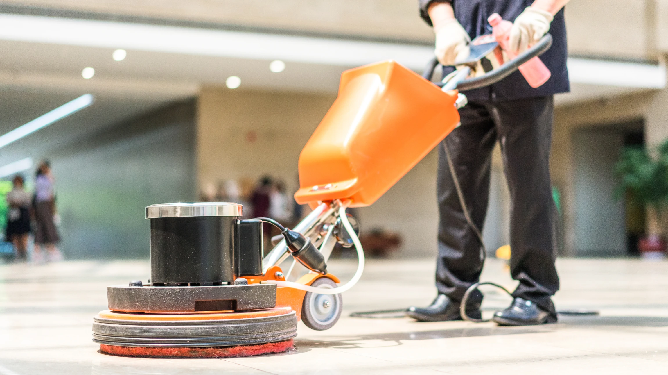 Opérateur en tenue professionnelle utilisant une monobrosse industrielle pour nettoyer un sol carrelé en pierre naturelle dans un espace commercial intérieur